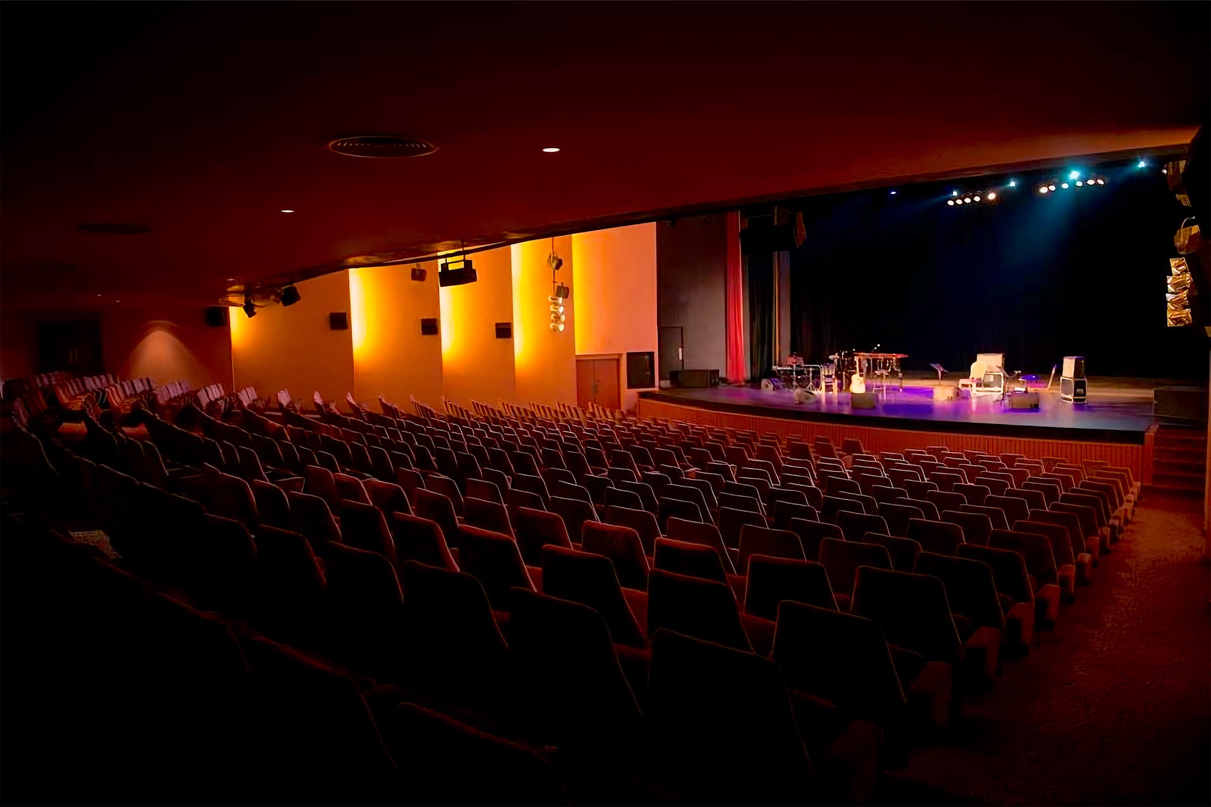 Rows of empty red seats in the Casino du Liban Theater facing the lit stage, instruments set and the curtain drawn back